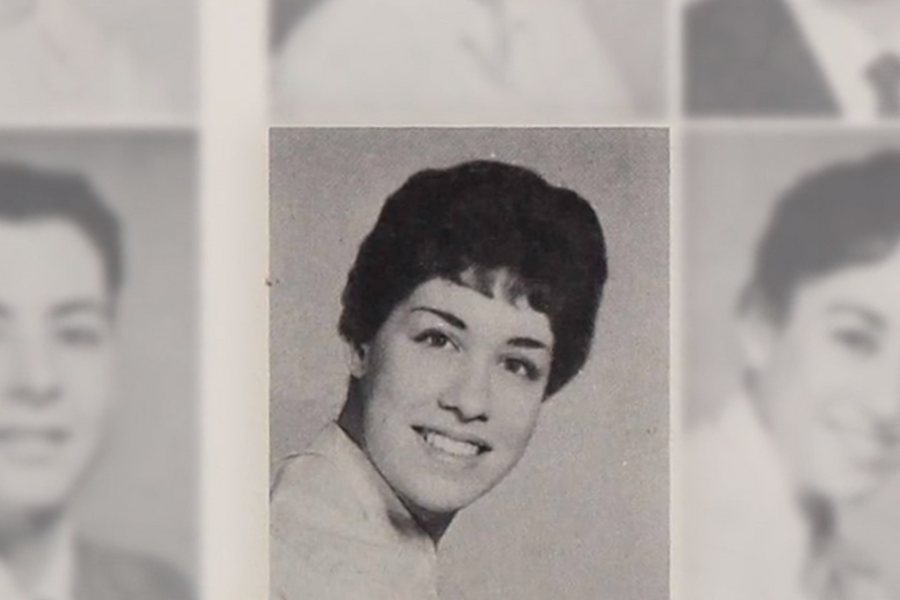 Black-and-white yearbook-style portrait of a young woman with short dark hair, smiling and wearing a light-colored collared blouse. The image is centered among other blurred portraits on a page.