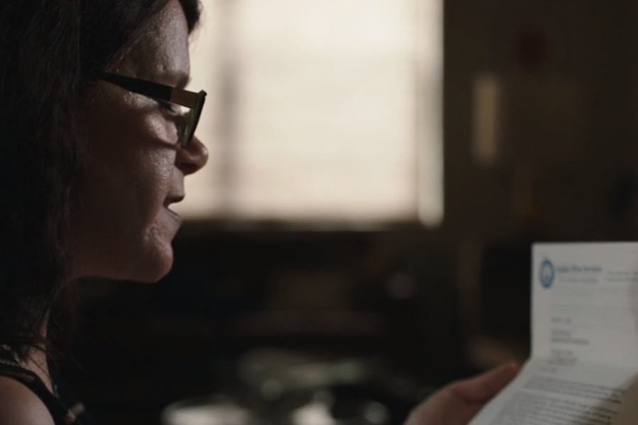 Side profile of a woman wearing glasses as she reads a formal letter, with soft lighting casting shadows on her face. The top corner of the document displays the Louise Wise Services letterhead, suggesting the content is significant or personal.