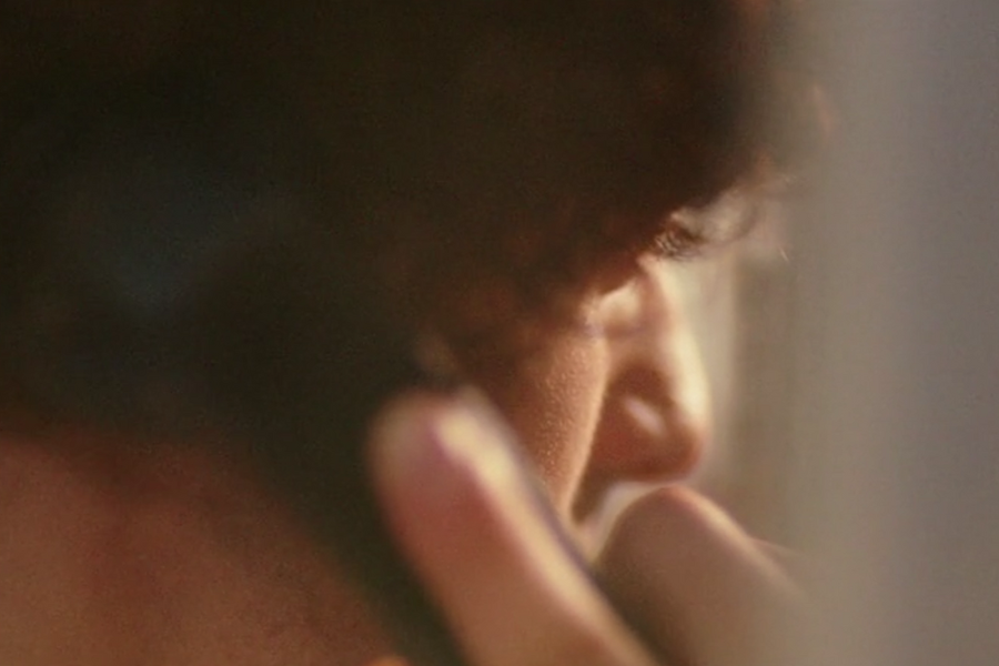Close-up shot of a person with curly hair speaking on a black corded phone, with soft focus highlighting their eye and contemplative expression.