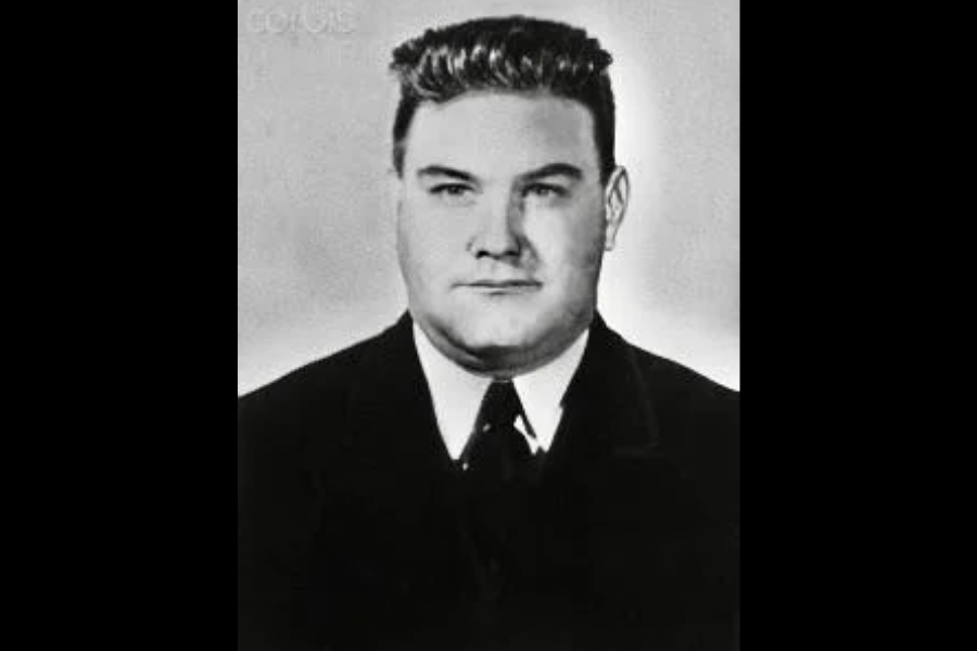 Black and white formal portrait of a young man with neatly styled hair, wearing a dark suit and tie. He’s facing forward with a composed expression against a light background.