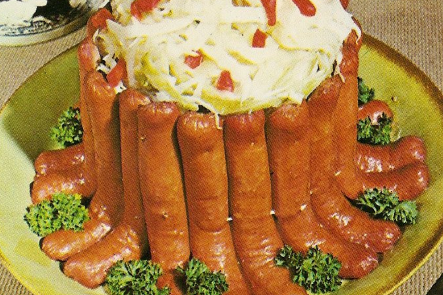 A retro dish shaped like a crown made from upright hot dogs, filled with shredded cabbage and pimentos, and garnished with parsley.