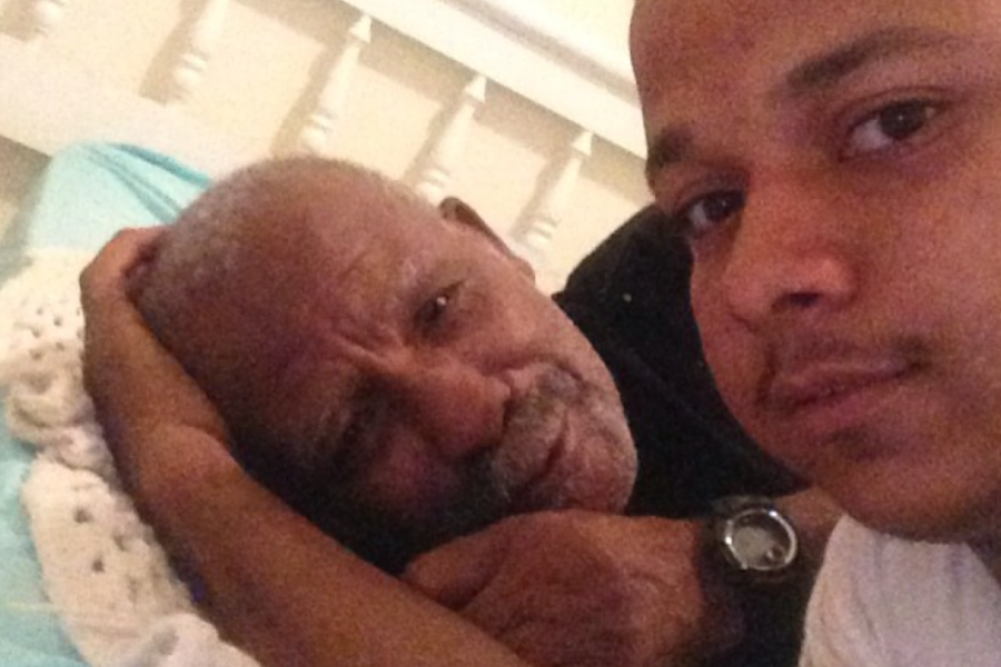A tender selfie of a young man lying next to an elderly man on a bed, sharing a quiet moment.