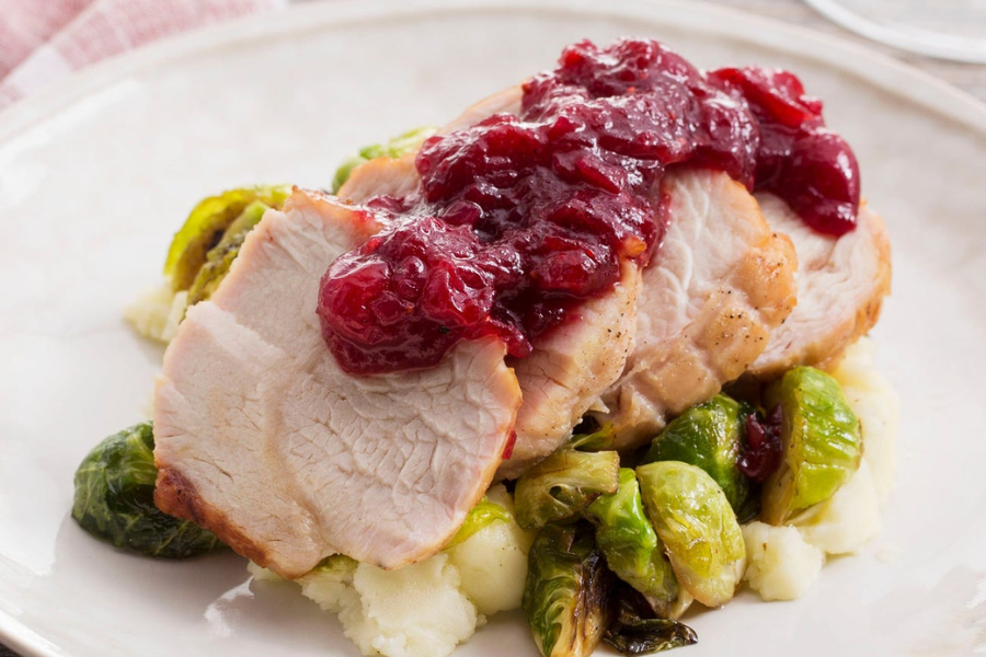Sliced roast turkey served on mashed potatoes and Brussels sprouts, topped with a generous portion of cranberry sauce.