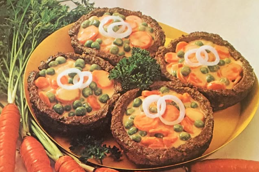 Four beef cup molds filled with a creamy carrot and pea mixture, topped with raw onion rings and surrounded by fresh parsley and whole carrots.