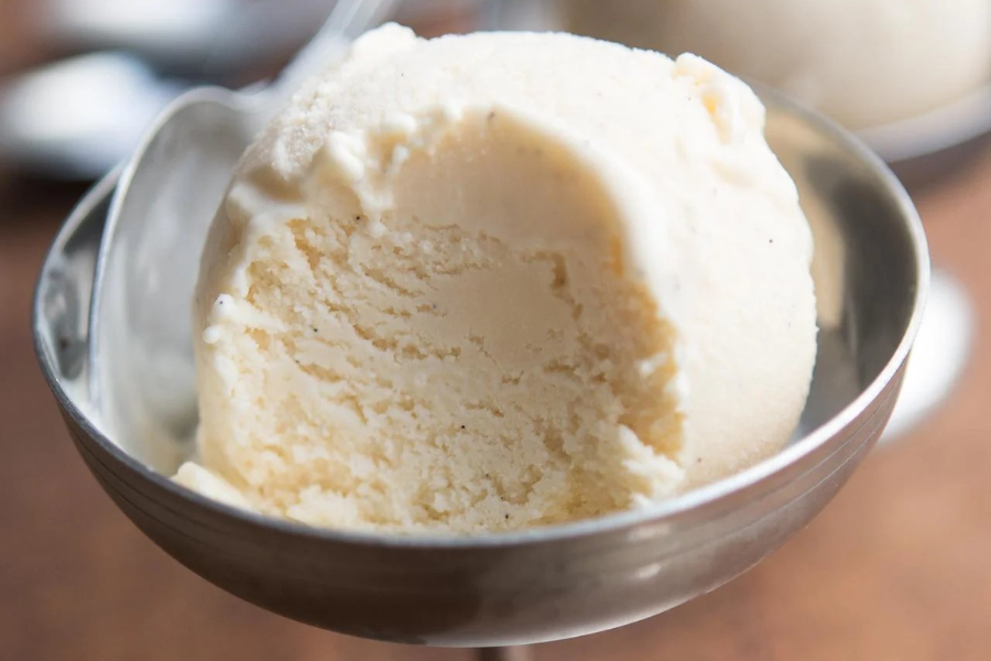 Close-up of a creamy scoop of vanilla ice cream in a silver dessert dish, showing a soft texture with specks of vanilla bean.
