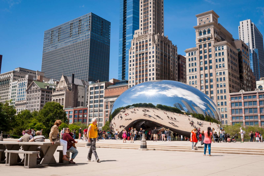 Tourists gather around Chicago’s reflective Cloud Gate sculpture in Millennium Park, with the city’s skyline towering in the background.