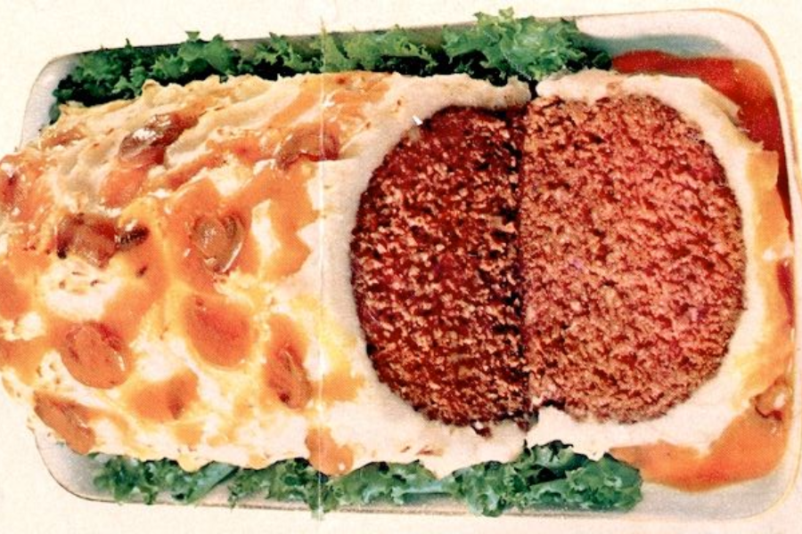 A meatloaf encased in mashed potatoes and topped with mushroom gravy, sliced to reveal the dense brown meat center.