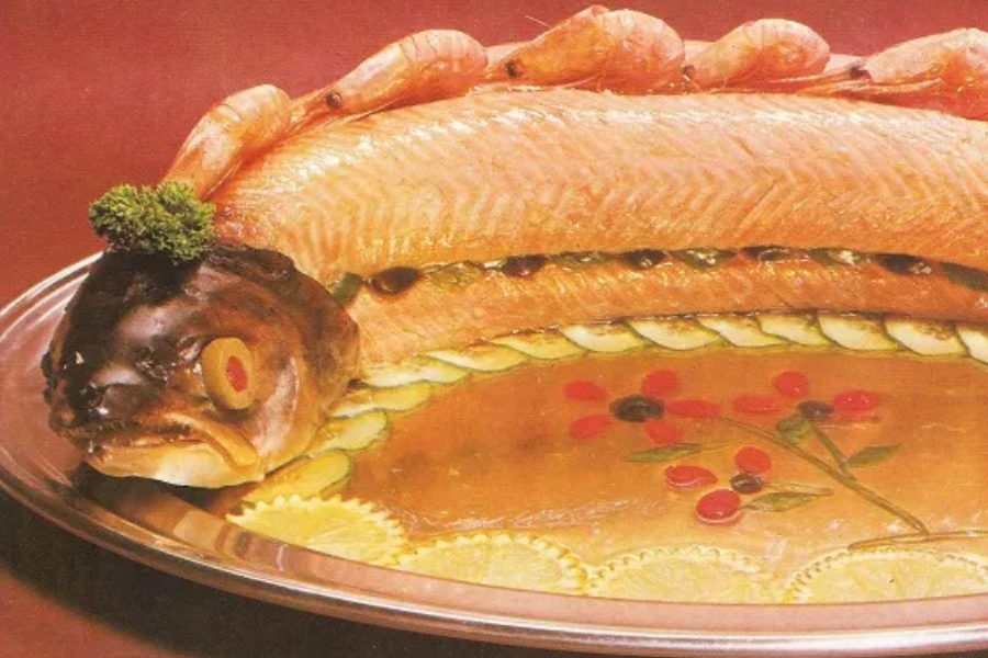 A large poached or gelatin-set fish laid out with its head intact, decorated with shrimp, cucumber slices, and parsley, served on a silver tray.