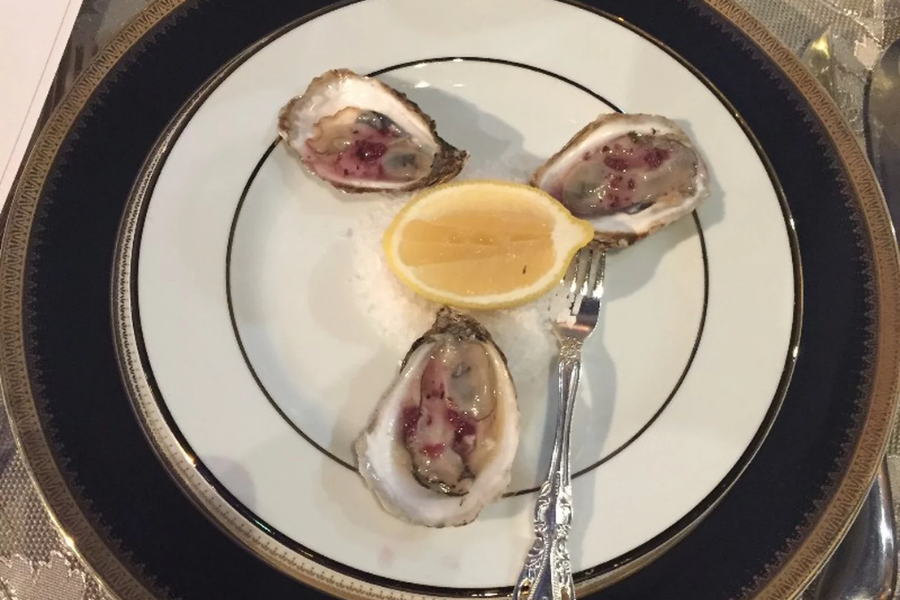 Three oysters on the half shell garnished with sauce, arranged around a lemon wedge on an elegant white and black-rimmed plate.