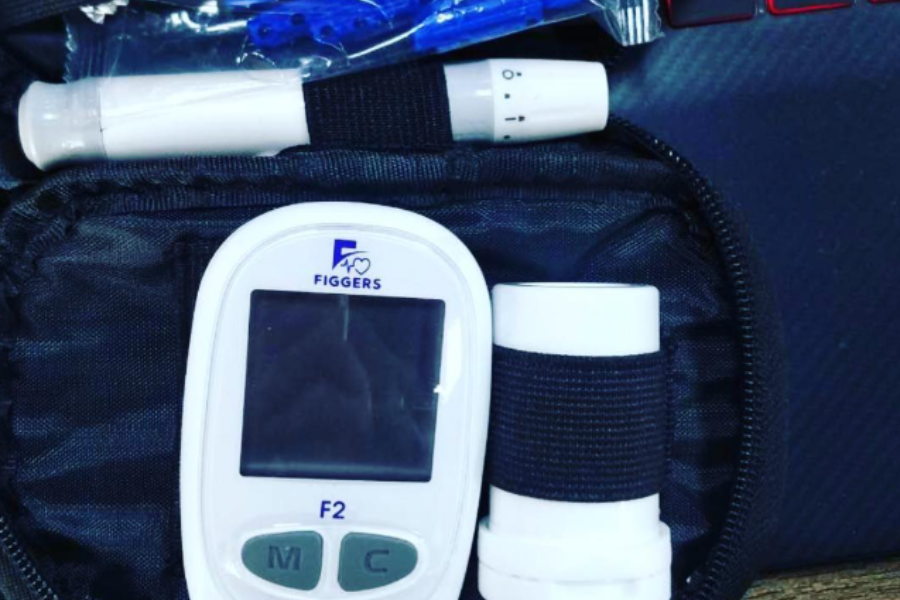 Close-up of a Figgers F2 medical device kit featuring a digital meter, lancets, and testing supplies inside a zippered case.