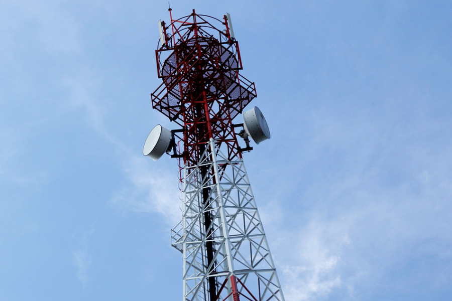 A red and white telecommunications tower stretches into the blue sky with large antennas mounted on the sides.