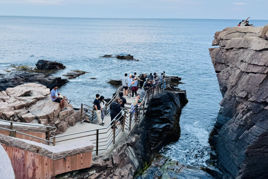 Tourists gather along a coastal walkway at Thunder Hole in Acadia National Park, watching the Atlantic waves crash against jagged rocks.
