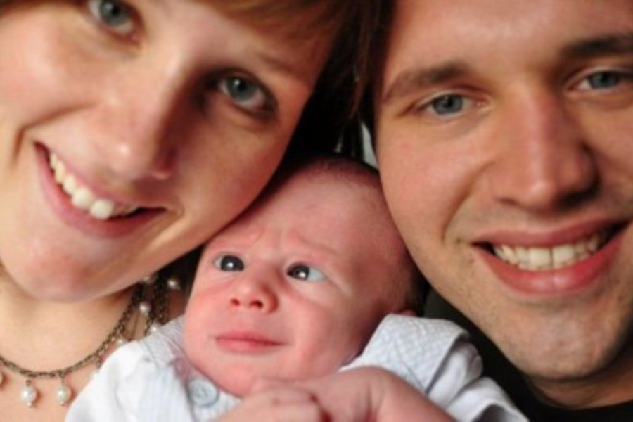 A close-up family selfie shows two smiling parents and a baby caught mid-expression looking extremely confused or concerned.