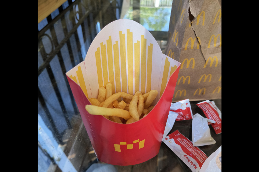 A red McDonald's fries container filled with French fries, with ketchup packets and a brown McDonald's bag in the background.