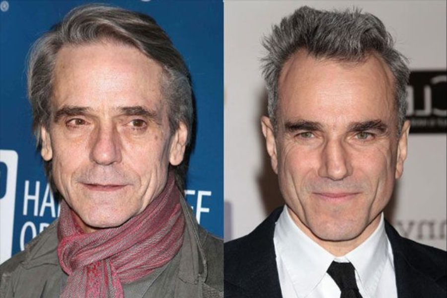 Side-by-side photo of two older men with gray hair wearing formal outfits. The man on the left has a scarf wrapped around his neck and a subtle smile, while the man on the right wears a black suit and tie, looking directly at the camera with a slight grin.