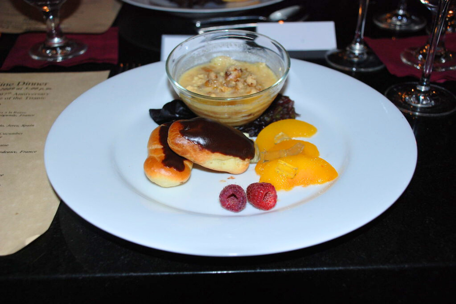 Dessert plate featuring chocolate-covered eclairs, poached peaches, raspberries, and a small bowl of Waldorf pudding from a Titanic-themed dinner.