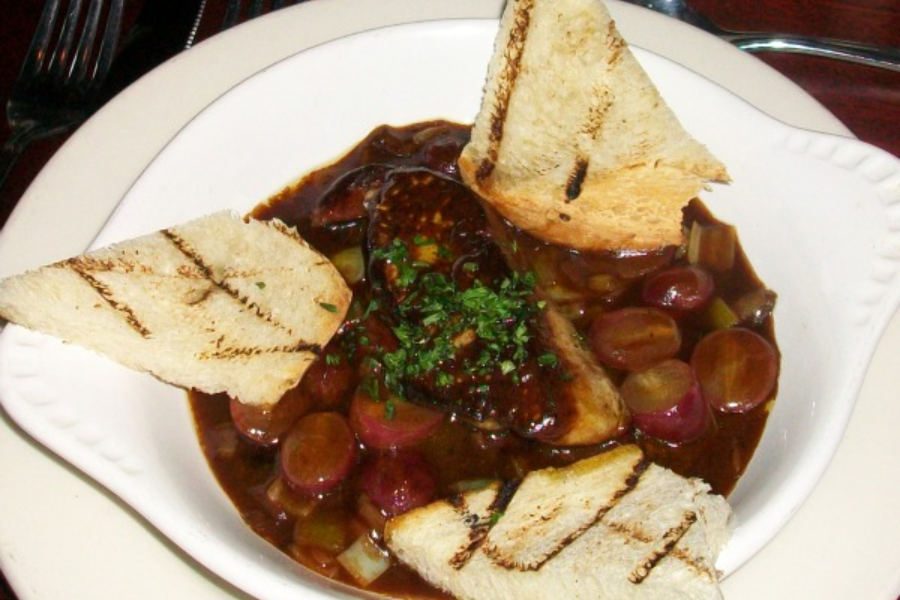 Dish of pâté de foie gras in a rich dark sauce with sliced grapes and garnished with chopped parsley, served with grilled toast points.