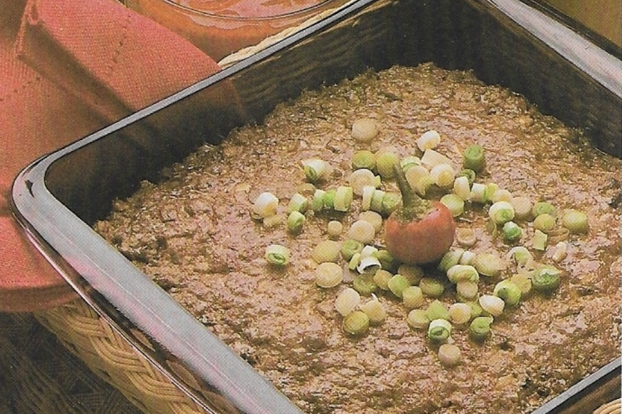 A square casserole dish filled with a thick brown meat mixture, garnished with chopped green onions and a whole red chili pepper in the center.