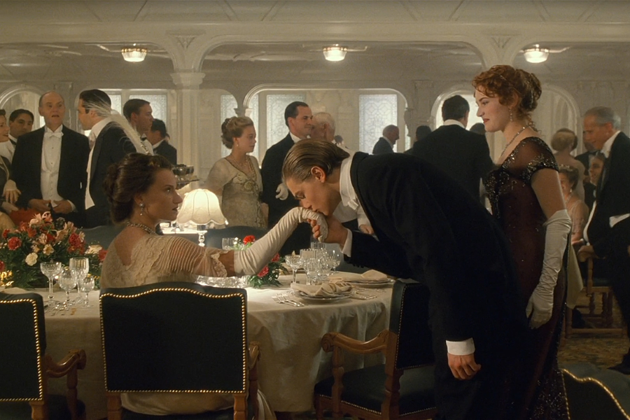 Scene from Titanic where Jack kisses a woman's hand while standing beside Rose in the opulent first-class dining room.