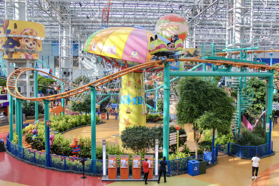 A vibrant indoor amusement park with a suspended roller coaster, colorful rides, and lush greenery inside the Nickelodeon Universe at the Mall of America.