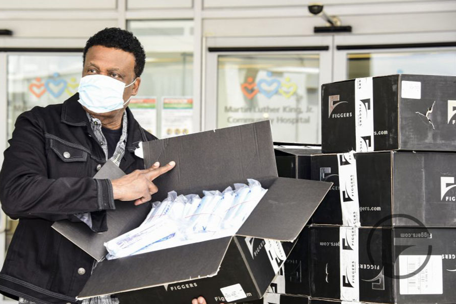 A man wearing a face mask unloads a box of individually wrapped items labeled “Figgers” outside Martin Luther King Jr. Community Hospital.