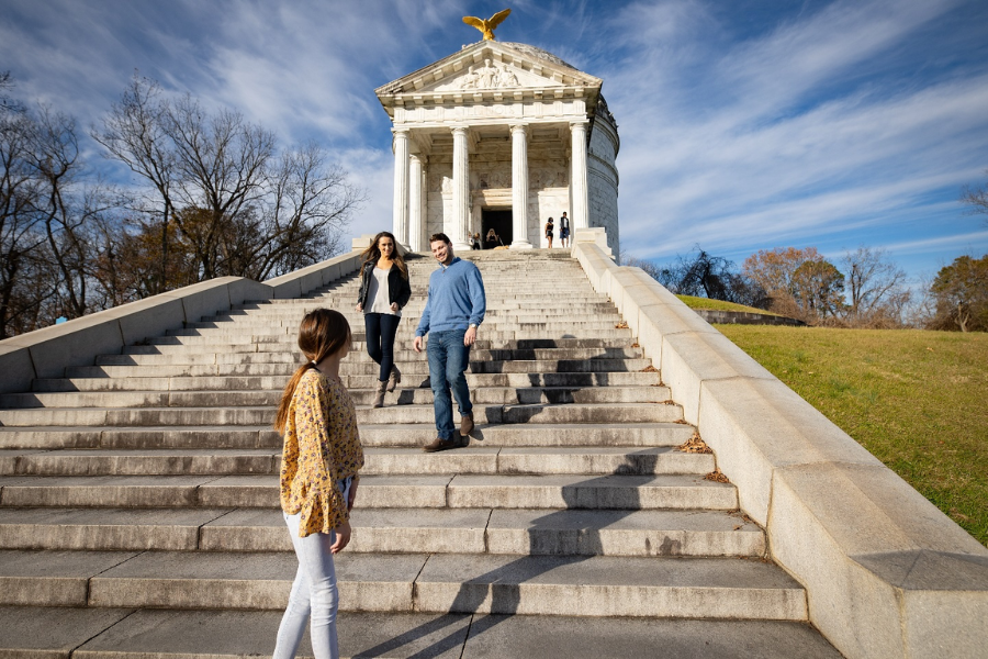 Visitors walk up the grand stone staircase to the Vicksburg National Military Park memorial, a neoclassical structure with tall columns and a golden eagle atop.