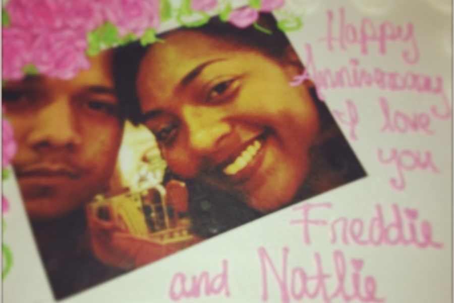 A close-up of a celebratory cake featuring a photo of a smiling couple with the handwritten message “Happy Anniversary I love you Freddie and Natalie.”