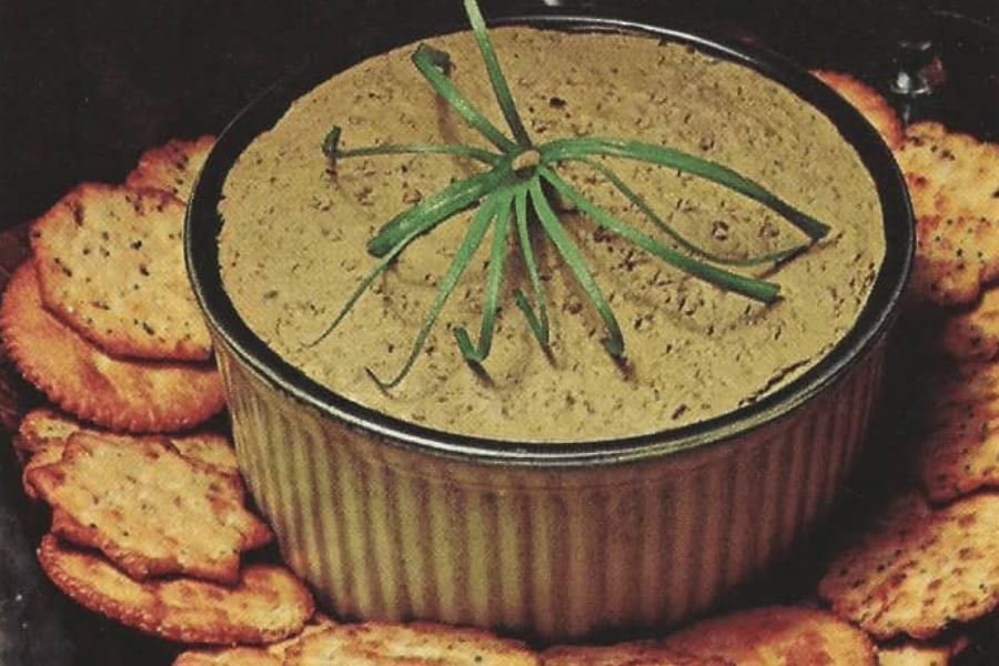 A ramekin of light brown pâté or spread topped with curled chives, surrounded by Ritz-style crackers.