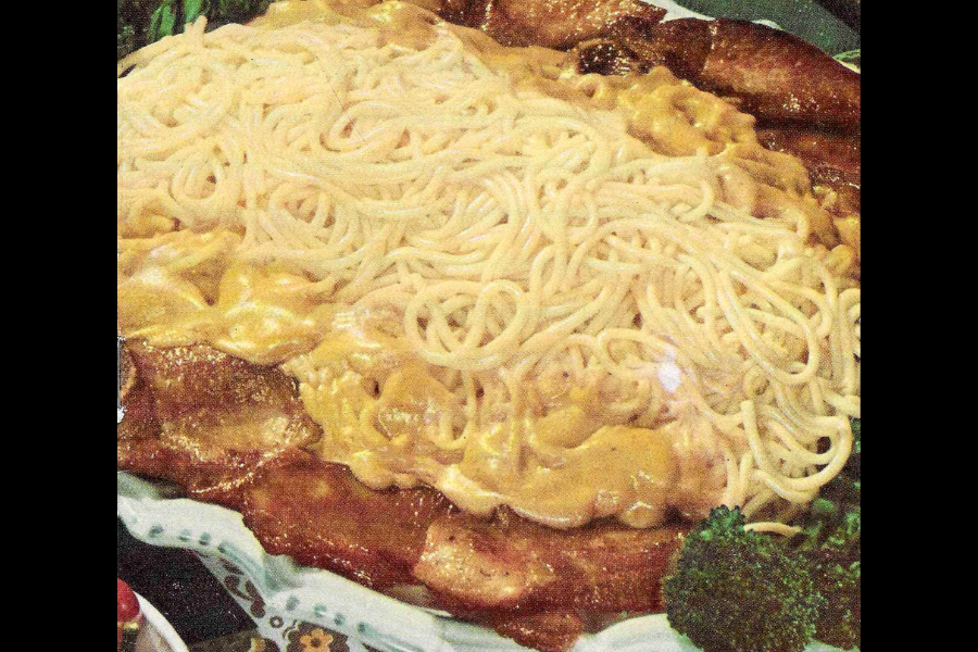 A plate of spaghetti noodles over creamy yellow sauce and slices of bacon, served with a side of steamed broccoli.