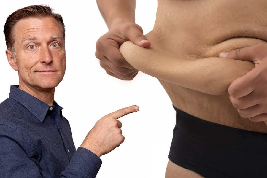 Man in a blue shirt pointing to loose belly skin being pinched by another person, highlighting weight loss or excess skin.