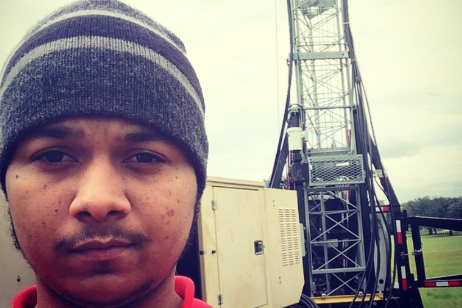 A man wearing a beanie stands in front of a mobile telecommunications unit with antenna towers and equipment mounted on a trailer.