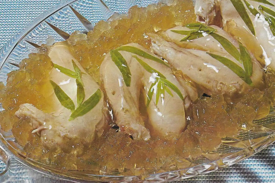 Poached chicken legs set in a clear aspic gelatin, garnished with fresh tarragon leaves and surrounded by crushed gelatin.