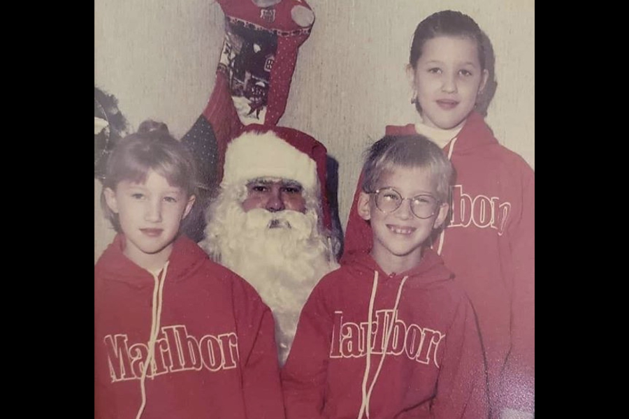 Three kids wearing bright red Marlboro-branded hoodies pose with Santa Claus in what looks like a home setting, creating an odd branding mix.