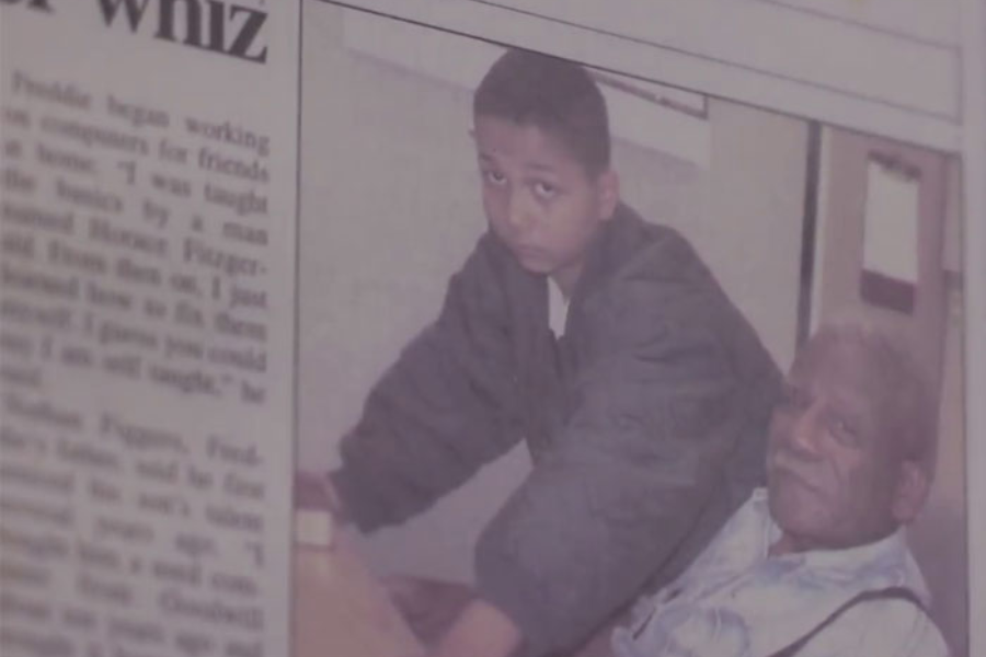 A newspaper photo showing a serious-looking boy sitting beside an elderly man, likely in a classroom or learning setting.