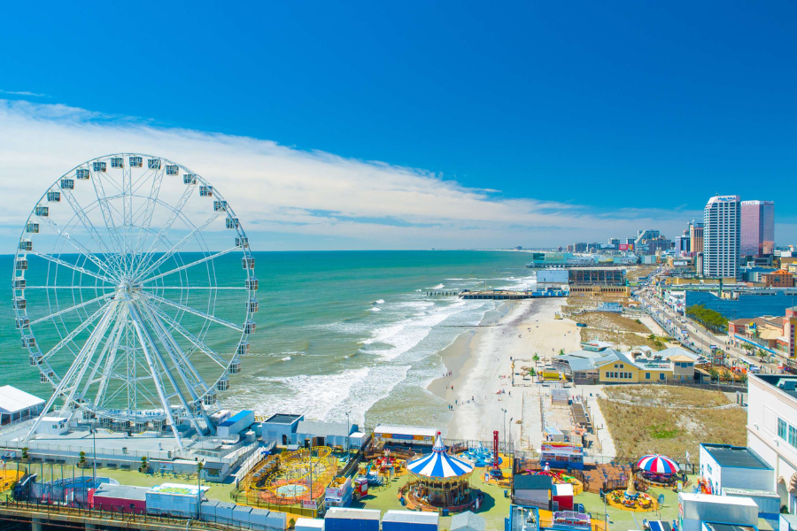 Aerial view of Atlantic City’s beachfront and boardwalk lined with casinos, amusement rides, and a large Ferris wheel next to the ocean.