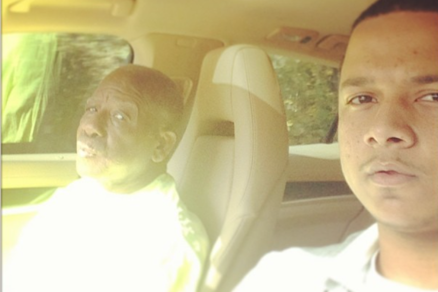 A selfie of a man and an elderly passenger sitting side-by-side in a car, softly lit by natural light through the window.