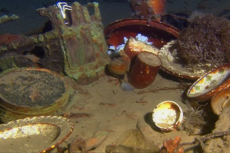 Underwater photo of Titanic wreckage showing intact and broken china dishes scattered on the seafloor among debris and marine growth.