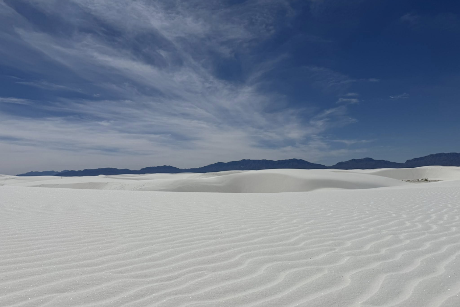 White sand dunes stretch across the horizon under a deep blue sky with wispy clouds at White Sands National Park in New Mexico.