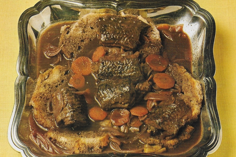 Lamprey Eel rolls in a thick brown gravy with sliced carrots and onions, served over pieces of bread in a silver-edged serving dish.