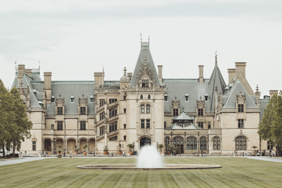 The grand Biltmore Estate in Asheville, North Carolina features elaborate stonework, tall towers, and a central fountain on its manicured lawn.