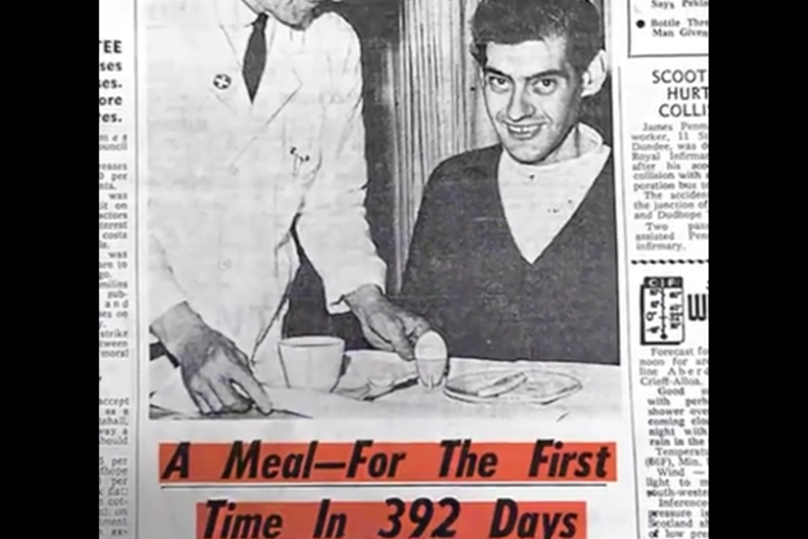 Newspaper clipping showing a smiling man seated at a table with a doctor serving him a small meal, with the headline “A Meal—For The First Time In 392 Days.”