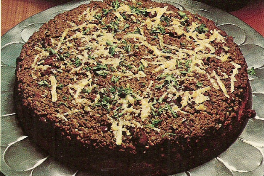 A round meatloaf-style dish topped with grated cheese and parsley, served on a silver platter in a cake-like presentation.