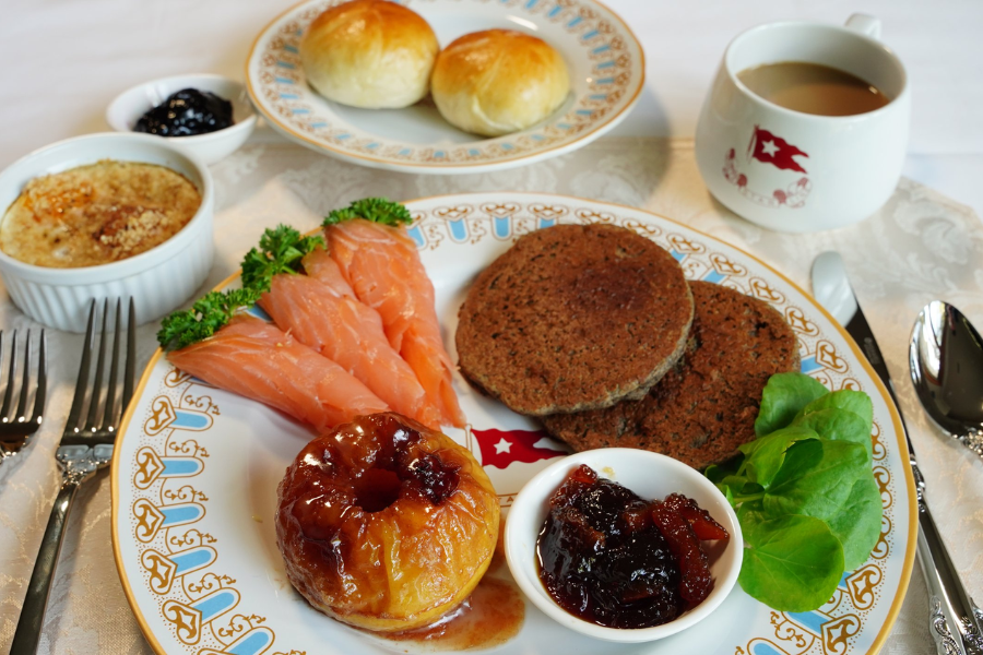Recreation of a Titanic first-class breakfast featuring smoked salmon, baked apple, buckwheat cakes, jam, and rolls, served on White Star Line china.