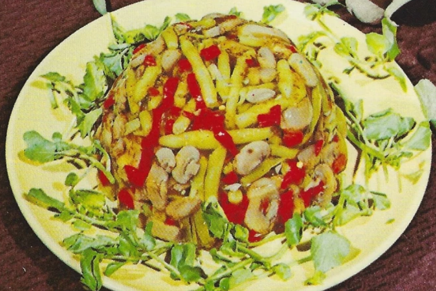 A dome-shaped vegetable aspic made with yellow wax beans, pimentos, and mushrooms, surrounded by watercress on a yellow plate.