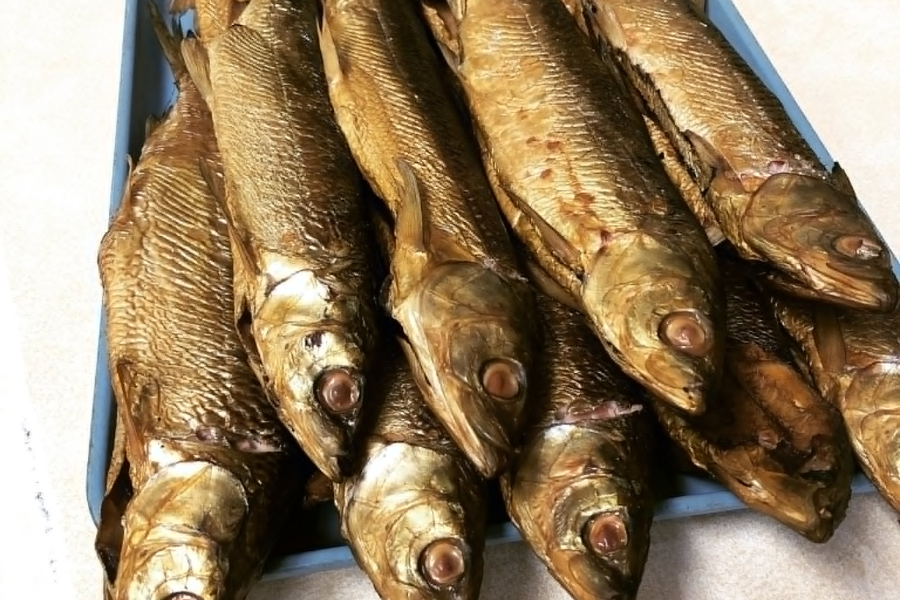 Close-up of a tray filled with whole smoked herrings, showcasing their golden, oily skin and preserved eyes.