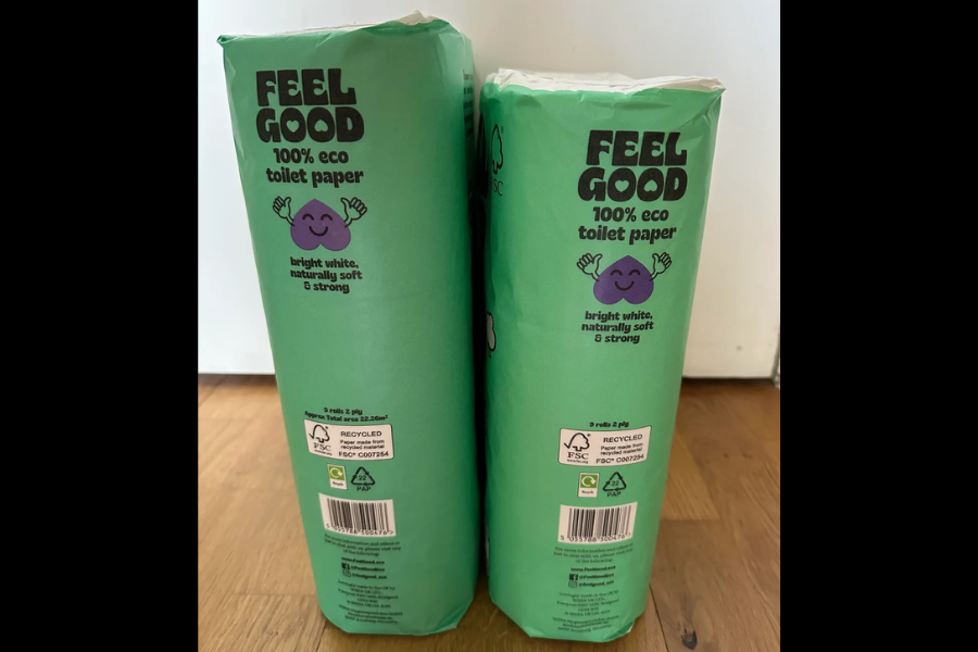 Two green packages of Feel Good 100% eco toilet paper, each featuring a smiling purple character and eco-friendly certifications.