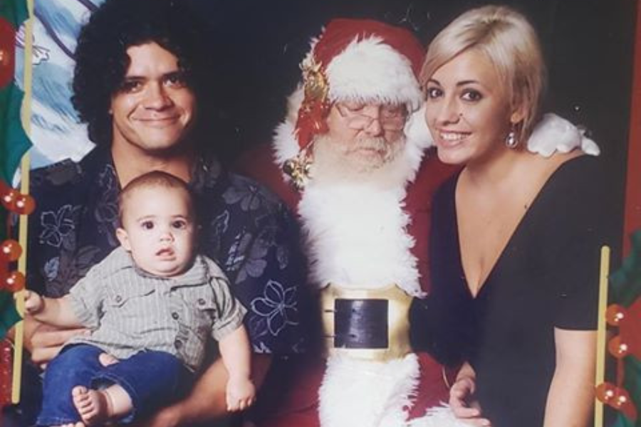 A family poses with Santa, but the baby looks dazed, the man smiles nervously, and Santa appears to be nuzzling the woman in an uncomfortable moment.