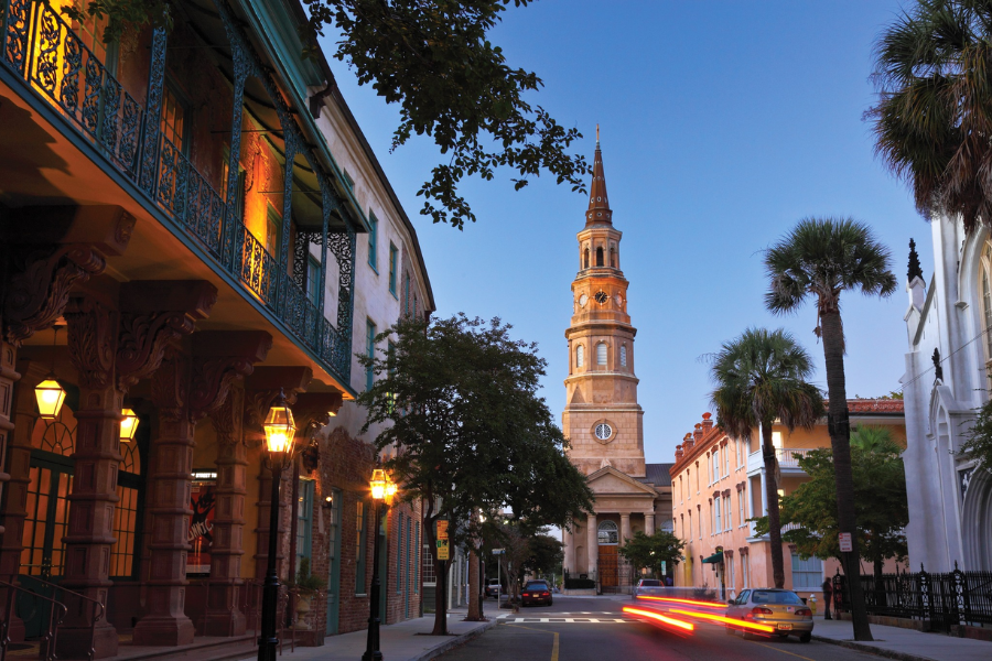St. Philip’s Church rises above a quiet, palm-lined street at twilight in Charleston’s historic district, surrounded by charming architecture and warm streetlights.
