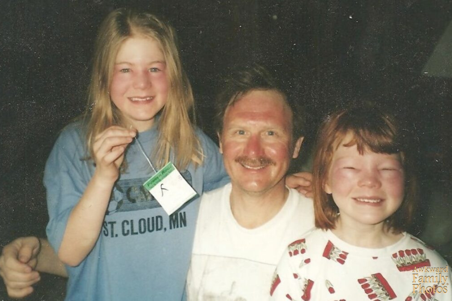 A smiling man poses with two young girls, all visibly sunburned—especially the girl on the right, whose eyes are nearly swollen shut.