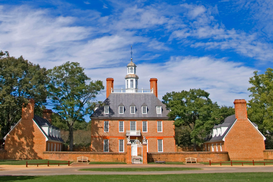 The Governor’s Palace in Colonial Williamsburg stands with its red brick facade, symmetrical wings, and a white cupola against a blue sky